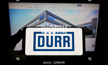 Person, die Smartphone mit Logo des deutschen Ingenieurunternehmens Dürr AG auf dem Bildschirm vor der Website hält. Konzentrieren Sie sich auf die Telefonanzeige. Stockfoto