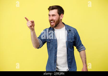 Lächelnder und gutaussehender Mann mit Stoppeln, der mit dem Finger auf gelben Hintergrund zeigt Stockfoto
