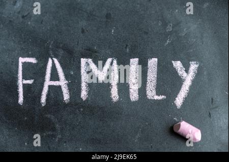 Familie. Ein Wort, das in rosa Kreide auf einer schwarzen Tafel geschrieben ist. Handgeschriebener Text. Daneben hängt ein Stück farbige Kreide. Stockfoto