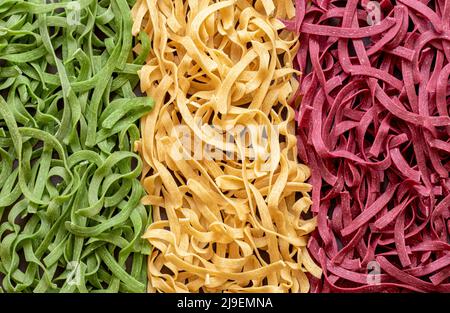 Oben mit dreifarbigen Nudeln, die als italienische Flagge angeordnet sind. Ungekochte Fettuccine-Pasta in drei Farben, hergestellt aus Spinat, roter Rübe und Knoblauch. Stockfoto