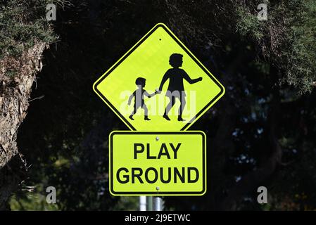 Ein Warnschild warnt den Fahrer, dass sich ein Spielplatz in der Nähe befindet, mit einem Symbol oder einer Grafik, die Mutter und Kind darstellt Stockfoto