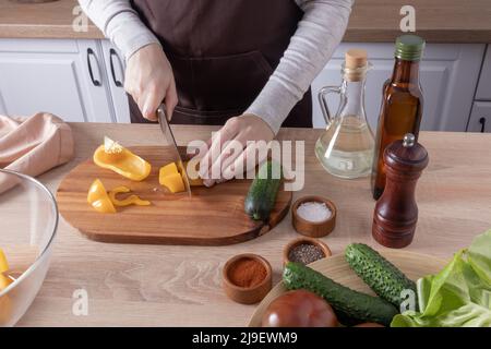 Kochen köstliche gesunde vegetarische Speisen in der Küche zu Hause. Die Hände des Mädchens schneiden frische Paprika auf einem Schneidebrett Stockfoto