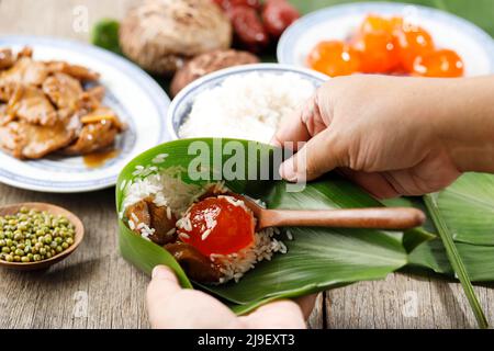 Lifestyle Shoot Reisknödel Bacang Zongzi Making, Wrapping Chinese Put Salted Egg Yolk on Ries for Dragon Boat Festival Feier, Close Up Stockfoto