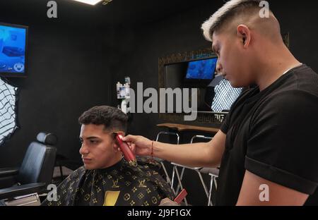 Junger Mann im Friseurladen, der im dunklen Vintage-Geschäft Haare schneidet Stockfoto