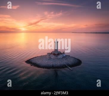 Leuchtturm auf einer kleinen Insel im Meer bei farbenfrohem Sonnenuntergang im Sommer Stockfoto