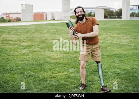 Junger Mann, der einen Teil seiner Beinprothese im Stadtpark hält - Fokus auf Hände, die Prothese halten Stockfoto