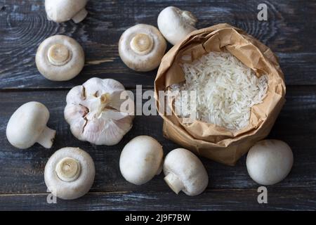 Zutaten für ein köstliches veganes Gericht. Weißer Basmati-Reis, Knoblauch und Champignons auf einem Holztisch, Draufsicht, horizontal Stockfoto