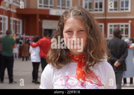 Schulschülerin in weißem Hemd mit blauen Augen trägt roten Schal Stockfoto