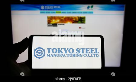 Person, die ein monbiles Telefon mit dem Logo des japanischen Unternehmens Tokyo Steel Co. Ltd auf dem Bildschirm vor der Business-Webseite hält. Konzentrieren Sie sich auf die Telefonanzeige. Stockfoto