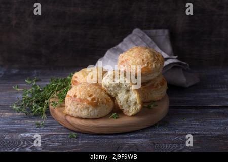 Hausgemachte, frisch gebackene Scones mit Käse und Kräutern auf Holzbrett auf Holztisch. Traditionelle englische Brötchen Stockfoto