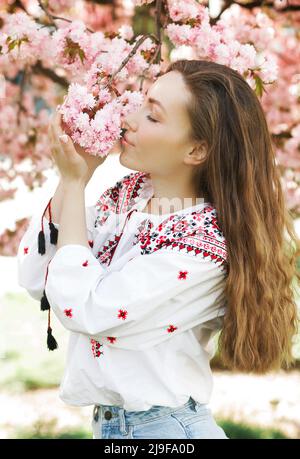 Porträt einer ukrainischen Frau in einem gestickten Hemd in der Nähe der blühenden Sakura im Park Stockfoto