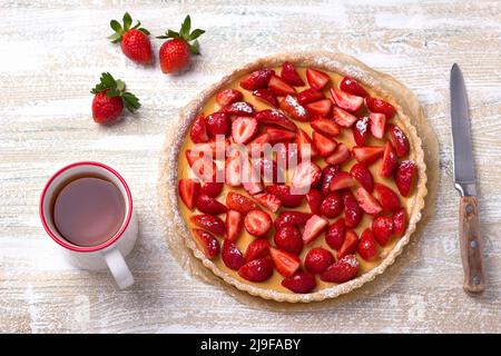 Sommertorte mit Pudding aus gebackener Milch, saftig frischen Erdbeeren und einer Tasse Tee auf hellem Holzhintergrund, Draufsicht, horizontal Stockfoto