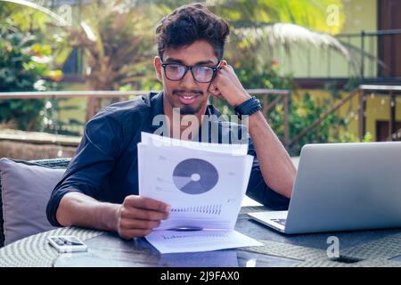 Schöner und junger erfolgreicher indischer Mann, der freiberuflich mit einem Laptop am Strand surft, vom ocean.india Geschäftsmann Freelance Stockfoto