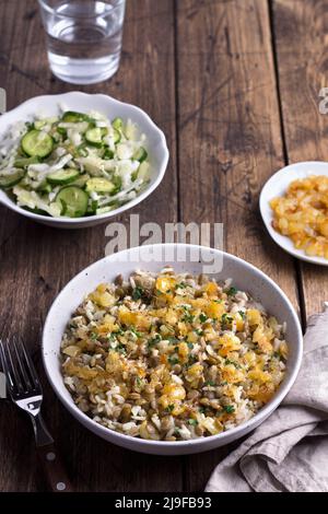 Traditionelles nahöstliches Gericht, Mujadara aus Linsen, Reis und gebratenen Zwiebeln mit einem Salat aus Kohl und Gurken auf Holztisch, Draufsicht, Platz, se Stockfoto