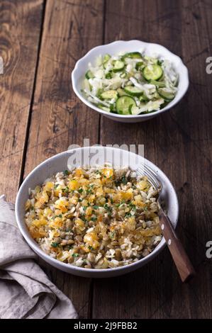 Traditionelles nahöstliches Gericht, Mujadara aus Linsen, Reis und gebratenen Zwiebeln mit einem Salat aus Kohl und Gurken auf Holztisch, Draufsicht, Platz, se Stockfoto