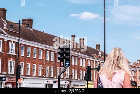 Epsom Surrey, London, Großbritannien, Mai 22 2022, eine anonyme Frau, die unter Blauem Himmel an einer Reihe von Geschäften und Apartments vorbeigeht und ein pinkes Top trägt Stockfoto