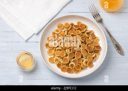 Teller Mini Pancakes Müsli mit Honig und frischem Orangensaft auf hellblauem Hintergrund. Trendige Küche. Hausgemachtes Frühstück. Draufsicht Stockfoto