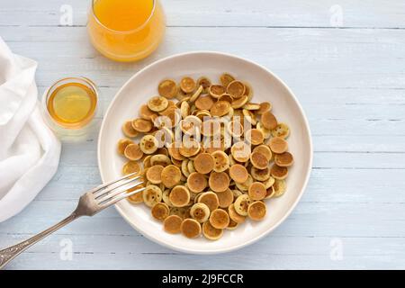 Teller Mini Pancakes Müsli mit Honig und frischem Orangensaft auf hellblauem Hintergrund. Trendige Küche. Hausgemachtes Frühstück. Draufsicht. Platz Stockfoto