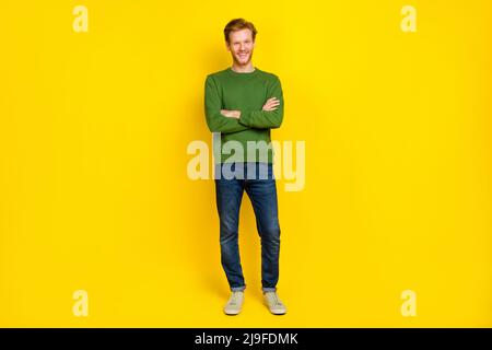 In voller Länge Foto von niedlichen attraktiven Kerl gekleidet grünen Pullover Arme gefaltet isoliert gelbe Farbe Hintergrund Stockfoto