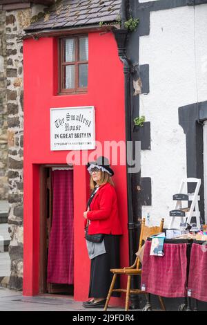 Weibliche Tourführerin in traditioneller walisischer Tracht, die vor dem kleinsten Haus in Großbritannien, Conwy, Wales, steht. Stockfoto