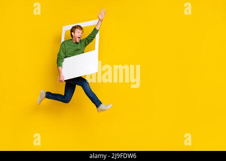 In voller Länge Foto von beeindruckt hübschen Mann tragen Pullover tacking Foto winken Arm leeren Raum isoliert gelben Hintergrund Stockfoto