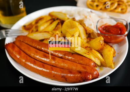 Deutsche Nationalkost. Teller mit leckeren Würstchen, Sauce und Flagge Deutschlands. Oktoberfest. Stockfoto