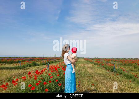 Mutter hält ihre Tochter auf einem Mohnfeld und blickt in die Ferne Stockfoto