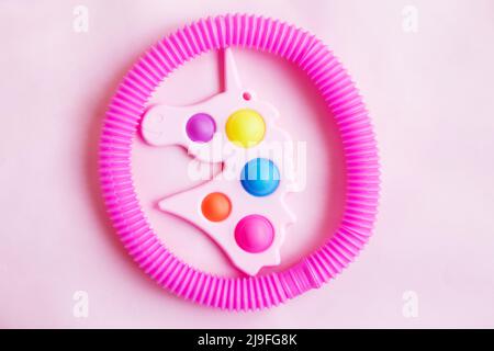 Einfache Grübchen in Form von Einhorn und einem Tubenfidget-Spielzeug auf einem rosa Hintergrund. Stockfoto