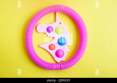 Einfache Grübchen in Form von Einhorn und einem Tubenfidget-Spielzeug auf gelbem Hintergrund. Stockfoto