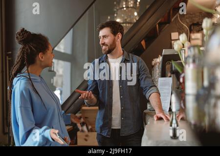 Ein junges Paar mit gemischter Rasse im Café, das Kaffee bestellt und lächelt. Luxuriöse Cafeteria. Auswahl von Getränken. Stockfoto