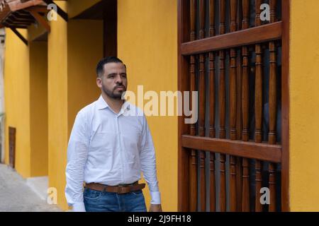 Porträt eines jungen Latinos in weiß gekleidet. Er geht die Straße seines Viertels in der Stadt entlang. Stockfoto