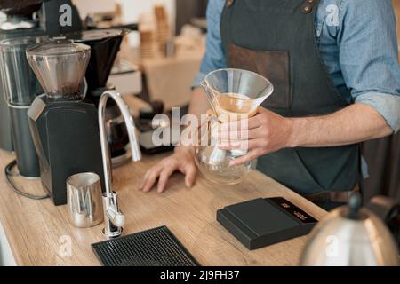 Der Barista hält in seinen Händen ein Glasgefäß für die Zubereitung von Filterkaffee Stockfoto