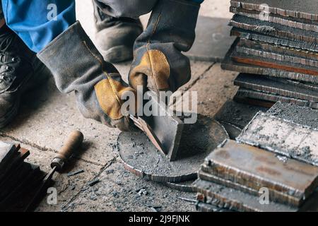 Arbeiter in der Schwerindustrie oder Metallurgie schlagen Eisenplatten mit Hammer ab. Arbeiten Sie mit Metall. Beschaffung von Wertstoffen für die Produktion. Authentischer Workflow. Stockfoto