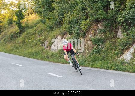 Professionelle Radrennfahrerin, die sehr schnell bergab und an einer Kurve fährt, auf einer Rennroute entlang der asphaltierten Forststraße Stockfoto