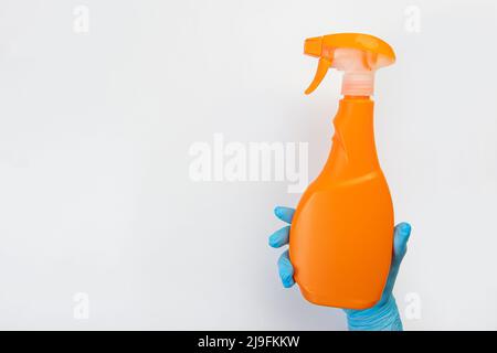 Die Hand einer Putzfrau in einem blauen Gummihandschuh hält eine Flasche Reinigungsmittel auf einem grauen Hintergrund. Reinigungsmittel für verschiedene Oberflächen in der Küche Stockfoto