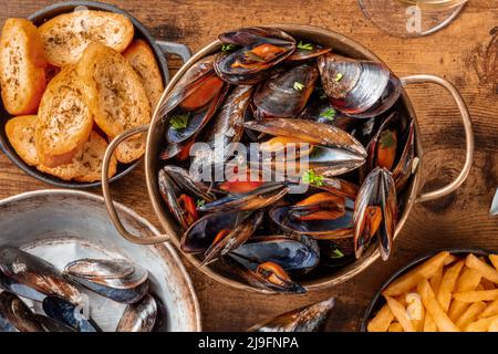 Belgische Muscheln mit Pommes frites und geröstetem Brot, über dem Kopf flach auf einem rustikalen Holzhintergrund Stockfoto