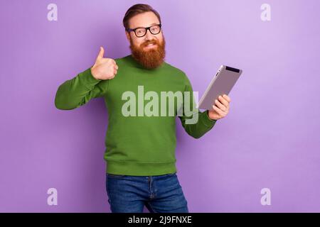 Foto von attraktiven jungen Freiberufler Kerl zeigt Daumen-up empfehlen Ihnen neue Tablet-Modell auf lila Hintergrund isoliert Stockfoto