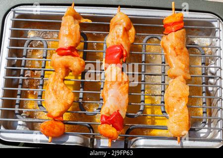 Drei rohe marinierte Hähnchenbroschette auf dem Gitter eines elektrischen Grills Stockfoto