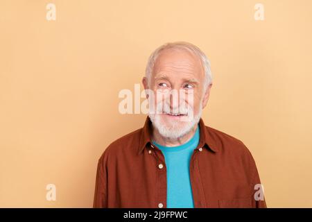 Foto von funky ältere graue Frisur Mann aussehen Werbung tragen braunes Hemd isoliert auf beige Hintergrund Stockfoto