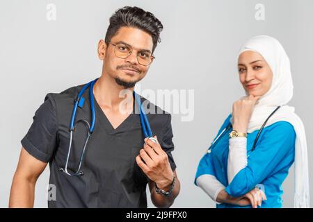 Schöne muslimische Ärztin und indische Krankenschwester in Brillen diskutieren Aufgaben. Porträt von schönen medizinischen Mitarbeitern mit Stethoskopen. Medizinische Hilfe, Insura Stockfoto