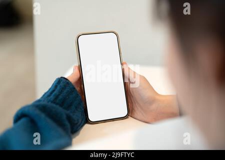 Junge Frau mit Smartphone leerem Bildschirm rahmenloses modernes Design, während sie auf dem Bett in der häuslichen Einrichtung liegt Stockfoto