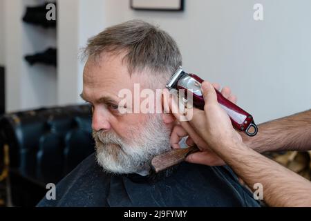 Ein alter Mann, der in einem Friseurladen einen Haarschnitt von einem Meister genießt. Ein alter Mann bekommt einen stylischen Haarschnitt Stockfoto