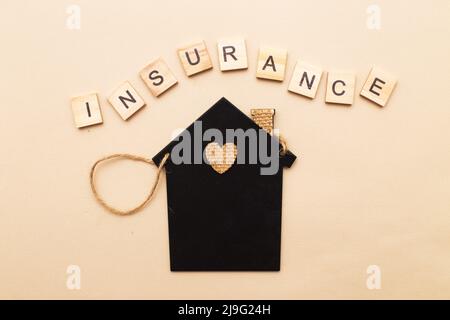 Inschrift Versicherung mit einem kleinen Haus auf beigem Hintergrund aus Holzblöcken. Stockfoto