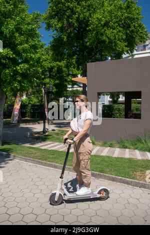 Junge Frau sitzt auf ihrem ständigen Elektroroller Stockfoto