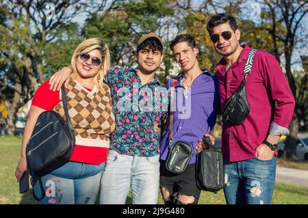 Porträt junger lateinamerikanischer argentinischer Freunde, die umarmt im Freien stehen und die Kamera betrachten, von der Sonne beleuchtet, in lässiger Kleidung gekleidet. Stockfoto