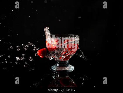 Erdbeeren fallen in ein Glas Wasser mit einem Spritzer auf schwarzem Hintergrund Stockfoto