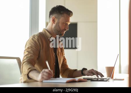Geschäftsmann, Der Mit Einem Laptop Arbeitet, Notizen Am Arbeitsplatz Machen, Seitenansicht Stockfoto