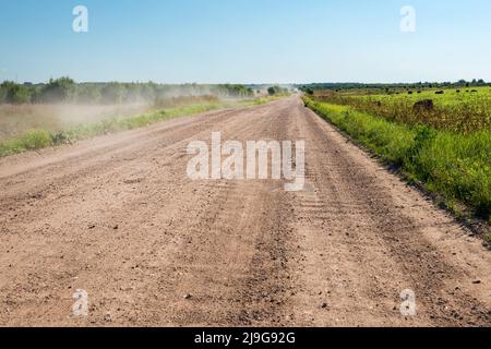 Die ländliche nicht asphaltierte Straße, die durch das landwirtschaftliche Feld geht Stockfoto