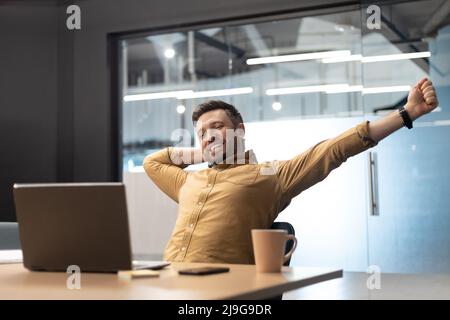 Zufriedener Geschäftsmann In Der Nähe Von Laptop Stretching Arms Entspannendes Sitzen Im Büro Stockfoto