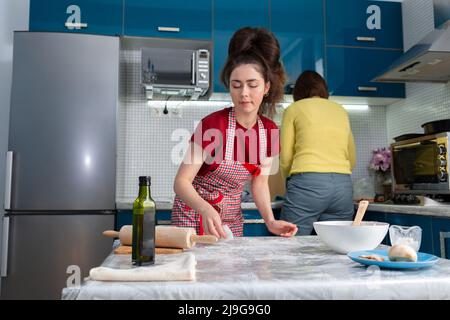 Zwei schöne junge Frauen bereiten gemeinsam in der Küche Essen zu. Reinigungs- und Reinigungsarbeiten. Stockfoto